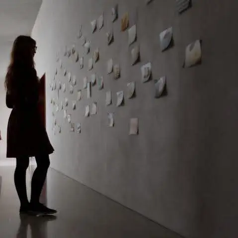 Elodie, en silhouette, regarde un mur couvert de petites images épinglées.